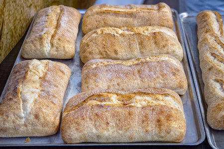 Fresh crispy ciabattas on metal tray on table in bakery, top view. Sale of baked goods in the store.
