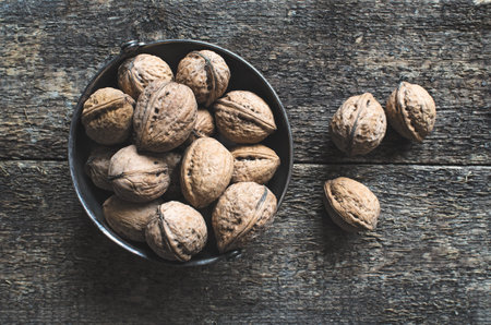 Whole walnuts in a metal bowl on a wooden rustic background, top view.