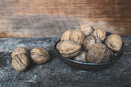 Whole walnuts in a metal bowl on a wooden rustic background.