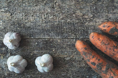 Organic garlic and dirty carrot whole on the wooden rustic background, top view. Vegetable.の写真素材