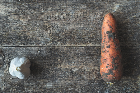 Organic garlic and dirty carrot whole on the wooden rustic background, top view. Vegetable.の写真素材
