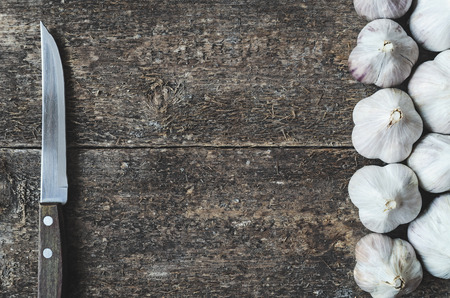 Organic garlic whole and kitchen knife on the wooden rustic background, top view. Garlic and knife Background. Vegetable.の写真素材