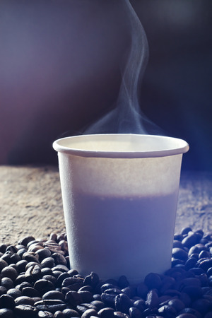 Paper cup of fresh hot coffee with smoke and coffee beans on wooden table.の写真素材