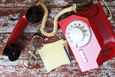 Red vintage phone on wooden background with pencil and glasses close-up, top viewの写真素材