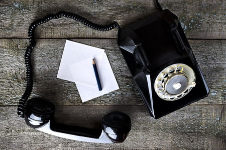 Black vintage phone on wooden background with pencil close-up, top view, pick up the phoneの写真素材