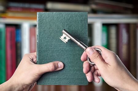 The book is the key to success, showing the green book and key to success in the hands against the background of shelves with books, copyspaceの写真素材