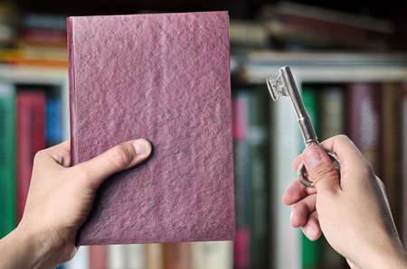 The book is the key to success, showing the red book and key to success in the hands against the background of shelves with books, copyspaceの写真素材