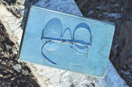Old spectacles or eyeglasses and vintage novel book on wooden surface in the park on sunny spring or autumn day, closeup outdoor, selective focus ,education conceptの写真素材