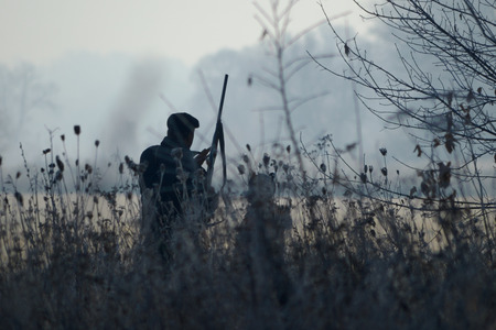 Silhouette of the two hunters at sunrise. Hunter man and boy during hunting period in search of wildfowl or game. Autumn hunting season. Grandfather teaches his grandson the hunting craftの写真素材