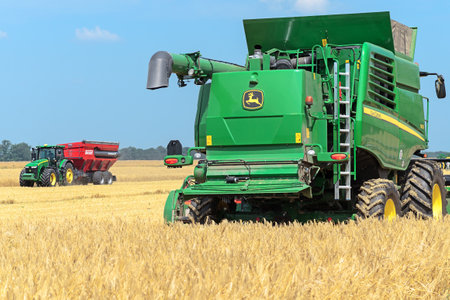 Kazanka, Ukraine - July 11: John Deere Combine Harvester T670 and Tractor 8370R Tractor using a bunker-reloader Perard Interbene 27 harvesting grain in the field near the village Kazanka, South Ukraine July 11, 2017のeditorial素材