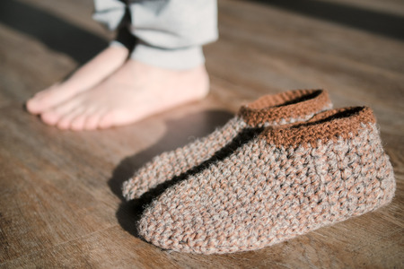 Feet of a woman in funny home made by hand slippers on the wooden warm floor background. Cozy home atmosphere. Warm floor heating concept. Close-up of female legs stepping by hardwood floor at homeの写真素材
