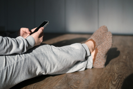 Woman sitting at cozy home interior and using modern smartphone device at sunset. Concept online shopping, texting message, searching information online, checking social networks, banking, making order on cell, close up.の写真素材