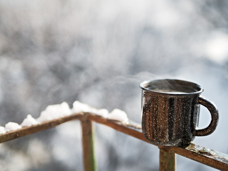 Cozy steaming cup with hot cocoa, tea or coffee. Mug winter morning or evening outdoors under snowfall. Winter and Christmas time concept.の写真素材