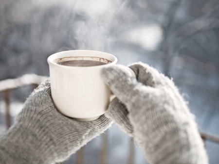 Woman hands in mittens holding a cozy steaming mug or cup with hot cocoa, tea or coffee. Beautiful...