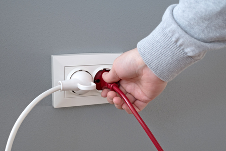 Hand plugging in an electric cord into a white plastic socket or  european wall outlet on grey plaster wall. Closeup of a woman's hand inserting an electrical plug into a wall socket. Daylight.の写真素材