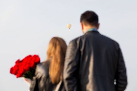 Loving couple man and woman with roses (in blur) on the background of a air balloon. Romantic date or wedding or valentines day concept. Selective focus.の写真素材