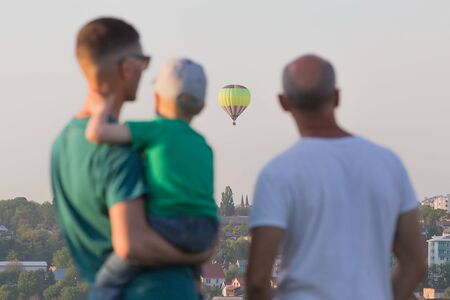 People watching the hot air balloons at the hill. Child looks curious a hot air balloon flying in the sky.の写真素材