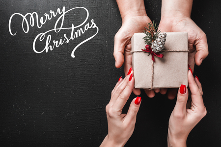 On a black background, a man's hands carry a gift in the hands of a young lady. Space for a greeting message with winter holidays. Top view.の写真素材