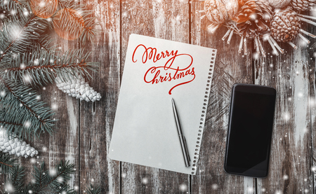 Old wood background, green fir tree with white cones, a cone basket, Merry Christmas message and phone. Greeting card space for winter holidays. Effect of snowflakes and light blips. Top view.の写真素材