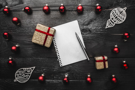 Upper, top, view from above of red evergreen toys, presents, handmade winter figurines, notepad and pen on black background, with space for text writing, greeting.の写真素材