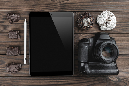 Workspace with tablet PC, camera and biscuits on wooden table. View from above, office table deskの写真素材