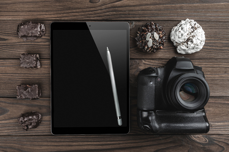 Top view of a camera photo, tablet in high definition with silver pen and sweets on a wood dark backgroundの写真素材
