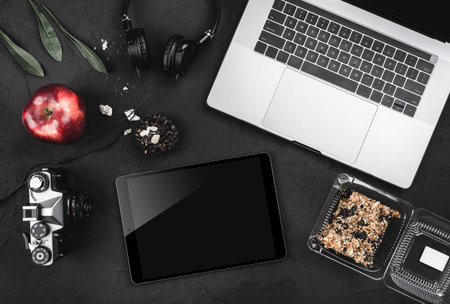 Open laptop with digital tablet, headphones, cookies and red apple on old stone desk. Top view, flat...