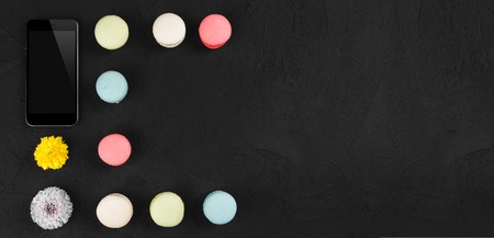 Tasty colorful macarons with phone and flowers on vintage stone background. Top view with copy space on the rightの写真素材