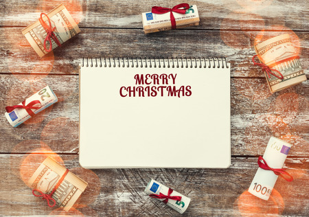 Xmas background of old wood. Gifts in American and European money. Text space in the notebook. Light effect.の写真素材