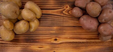 Heaps of two types of potatoes on dark wooden rustic table. Horizontal image with space for writingの写真素材