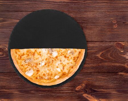 Half of pizza five cheeses on slate bottom, on wooden table, top view, space for textの写真素材