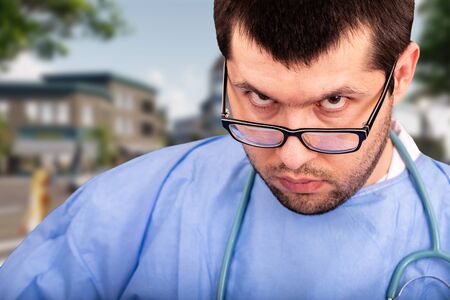 Young male doctor with stethoscope and glasses after a hard day at work in the hospital against the virus covid-19. The concept of stop the spread of the Coronavirusの写真素材