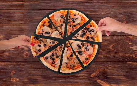 Young people taking slices of tasty pizza with ham, mozzarella, mushrooms and olives from the slate...