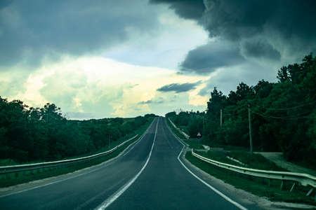 Asphalt road in countryside on at sunrise. Early in the morning the sun rises through the clouds. Forests in the moldovaの写真素材