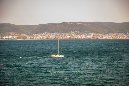 A yacht off the Mediterranean Sea, against the backdrop of a city and mountains