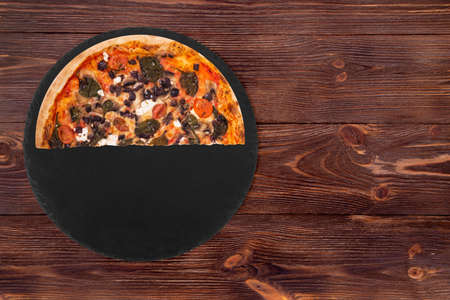 Half a pizza with cherry tomatoes, spinach, mozzarella, feta, kalamata olive and mushrooms on slate plate which is on wooden background, top view and space for textの写真素材