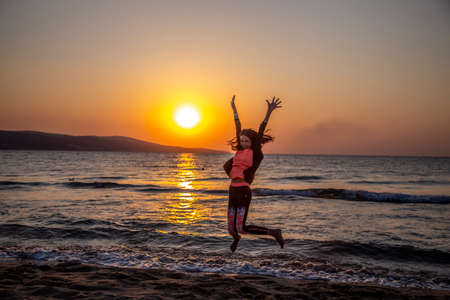 Happy woman jumping and enjoy life on the beach vacation at the sunrise. Early morning, the sun rises and shines in the seaの写真素材