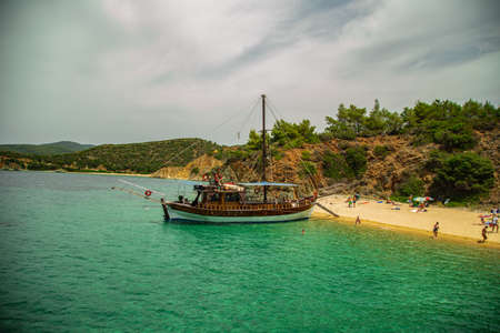 The wooden tourist boat or ship parked at the seaside. Amazing landscape view of the golden sandy beach, azure sea water and rocks covered with forestsの写真素材