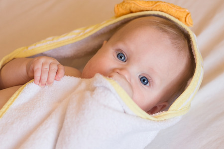 Adorable baby, looking out under a white and yellow blanket, towelの写真素材