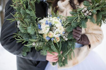 Beautiful wedding bouquet in hands of the bride and groom with spruce scarf in winterの写真素材