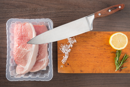 overhead view fresh packaged raw meat on old wooden cutting board with knife.の写真素材