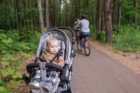 Baby in sitting stroller on nature. Adorable one year-old child with a stroller walk in a green summer forest on the bike pathの写真素材