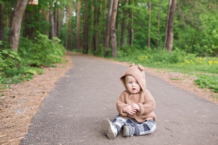 A one year old baby boy sitting outdoors in spring park. Cute toddler walking in the green forest in summerの写真素材