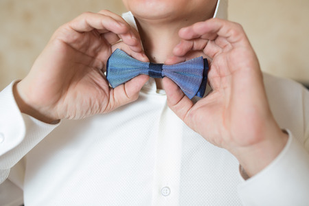 Man's hands touches blue bow-tie in the cage on a white shirt.の写真素材