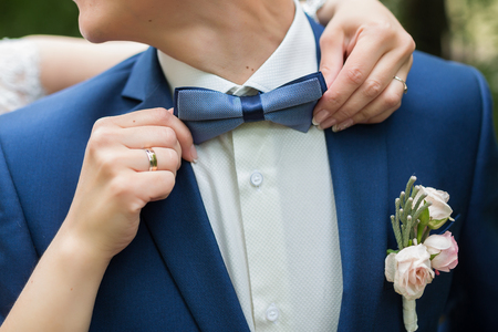 Man's hands touches blue bow-tie in the cage on a white shirt and suit.の写真素材