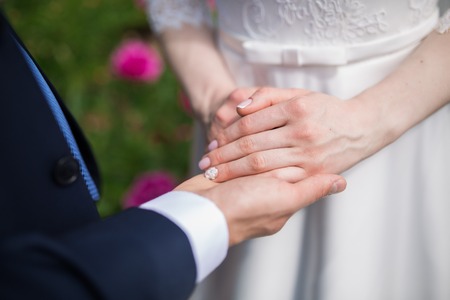 A newly couple place their hands on a wedding bouquet showing off their wedding rings.の写真素材