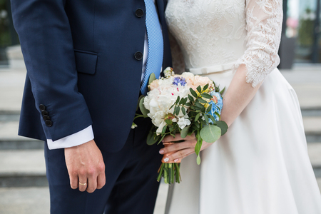 Wedding couple holding hands on summer green background with Rich bunch of pink peonies and lilac eustoma roses flowers. Wedding concept with bouquetの写真素材