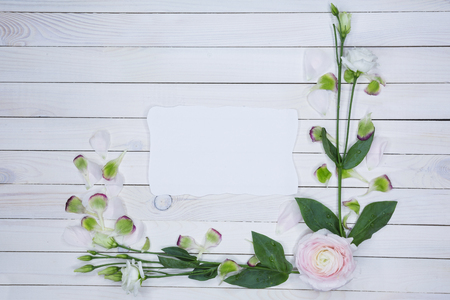Top overhead view of floral wreath frame with roses, ranunkulyus, branches, leaves and petals isolated on Vintage white wooden background with free a sheet of paper for text. Free text space concept. Beautiful romantic composition with flowersの写真素材