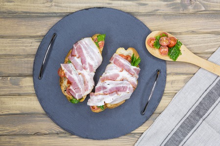 Bruschetta with bacon, tomatoes, herbs and oil on toasted garlic cheese bread ciabatta. Top view of of a girl taking a sandwich hand, flat layの写真素材