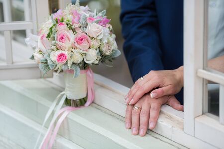 Wedding couple holding hands on summer green background with Rich bunch of pink peonies and lilac eustoma roses flowers. Wedding concept with bouquetの写真素材